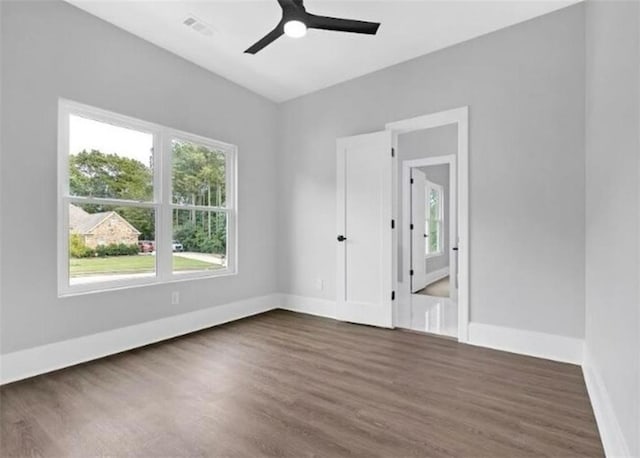 spare room featuring dark wood-style flooring, a ceiling fan, visible vents, and baseboards
