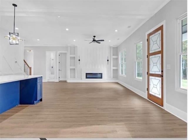 unfurnished living room featuring a ceiling fan, baseboards, light wood finished floors, a glass covered fireplace, and recessed lighting