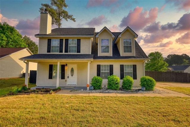 traditional home with a chimney, stucco siding, covered porch, fence, and a lawn