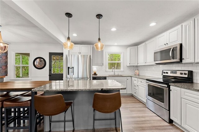 kitchen with a kitchen breakfast bar, white cabinetry, a kitchen island, appliances with stainless steel finishes, and a sink