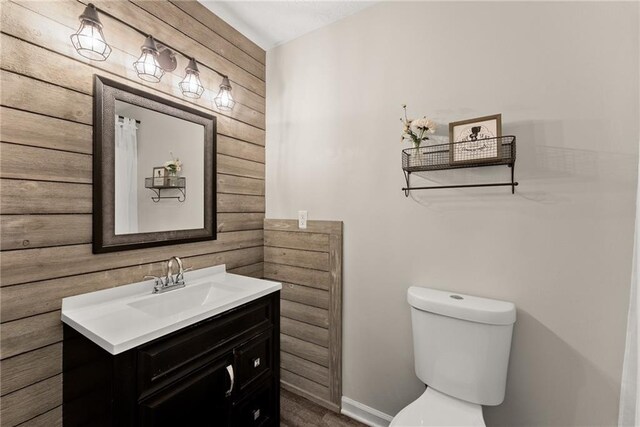 half bathroom featuring wood walls, toilet, vanity, and baseboards