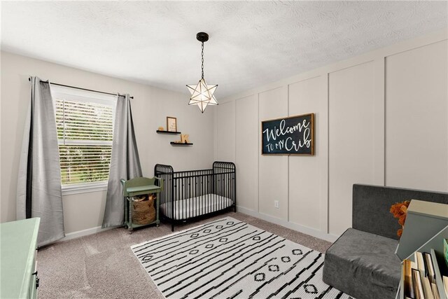 carpeted bedroom with a textured ceiling, a decorative wall, and a nursery area
