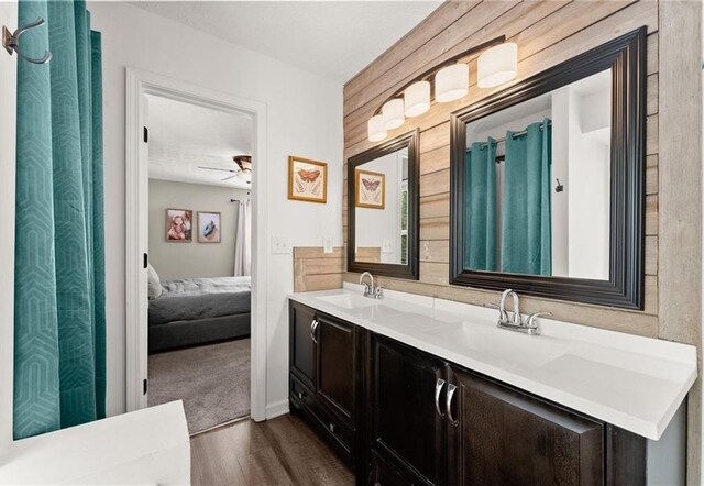 ensuite bathroom featuring double vanity, ceiling fan, a sink, and wood finished floors