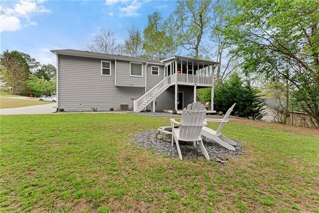 rear view of house featuring a sunroom, a lawn, a fire pit, and stairs
