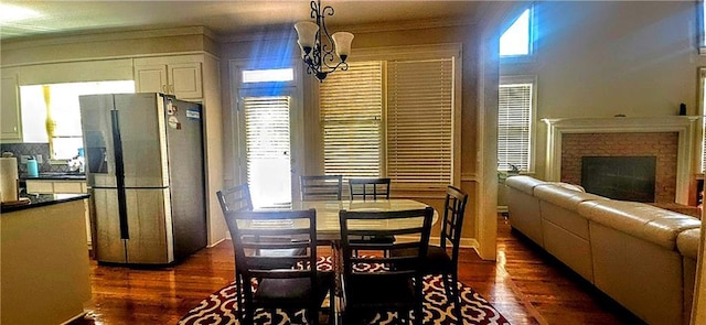 dining area with a chandelier, dark wood-style flooring, a brick fireplace, and crown molding