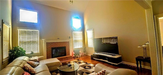 living area featuring baseboards, wood finished floors, a brick fireplace, and high vaulted ceiling