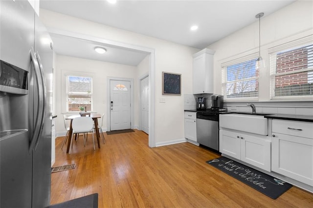 kitchen featuring sink, white cabinetry, light wood-type flooring, pendant lighting, and stainless steel appliances