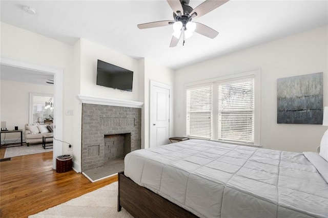 bedroom with wood-type flooring, a brick fireplace, and ceiling fan