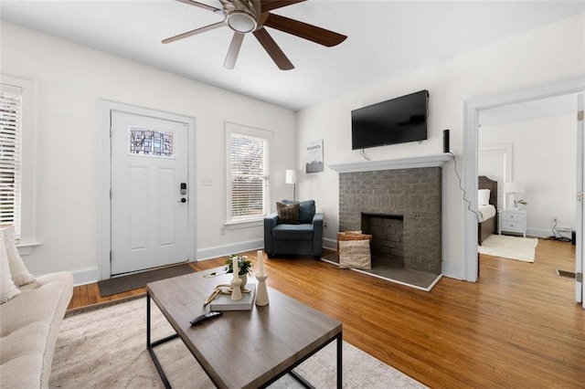 living room with a fireplace, ceiling fan, and light wood-type flooring