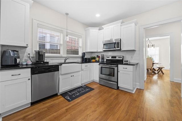 kitchen with appliances with stainless steel finishes, light hardwood / wood-style flooring, hanging light fixtures, and white cabinets