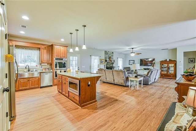 kitchen with appliances with stainless steel finishes, sink, decorative light fixtures, light hardwood / wood-style floors, and a kitchen island