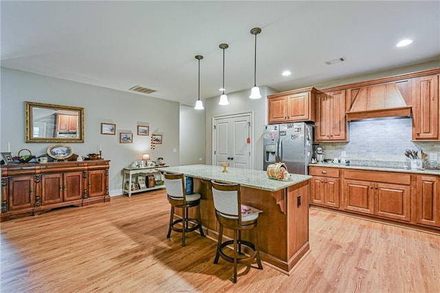 kitchen featuring stainless steel refrigerator with ice dispenser, premium range hood, light hardwood / wood-style flooring, a kitchen island, and a breakfast bar area