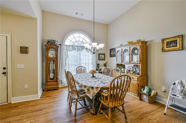 dining space featuring an inviting chandelier, high vaulted ceiling, and light hardwood / wood-style flooring