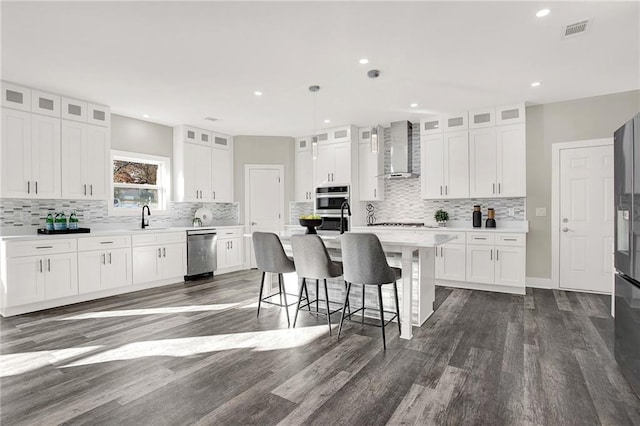 kitchen with white cabinets, wall chimney exhaust hood, dark hardwood / wood-style floors, and an island with sink