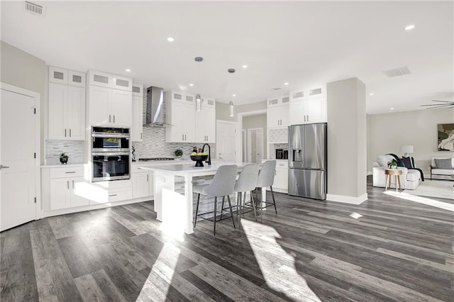 kitchen featuring wall chimney exhaust hood, stainless steel appliances, dark hardwood / wood-style flooring, a kitchen island with sink, and white cabinets