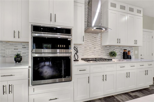 kitchen featuring tasteful backsplash, white cabinetry, wall chimney exhaust hood, and stainless steel appliances