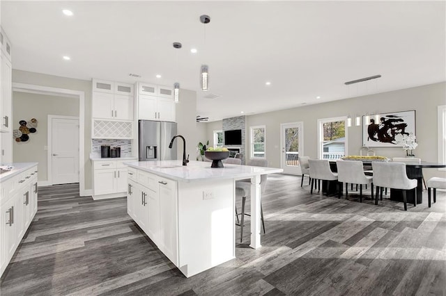 kitchen featuring pendant lighting, white cabinets, stainless steel refrigerator with ice dispenser, dark hardwood / wood-style floors, and an island with sink