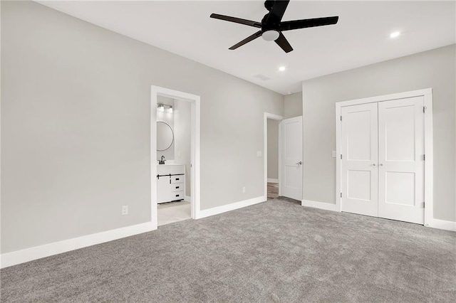 unfurnished bedroom featuring ensuite bath, light colored carpet, ceiling fan, sink, and a closet