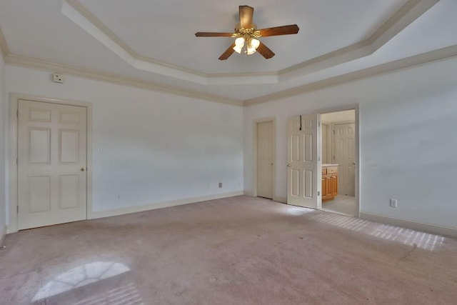 unfurnished bedroom featuring ceiling fan, a raised ceiling, carpet, ensuite bath, and ornamental molding