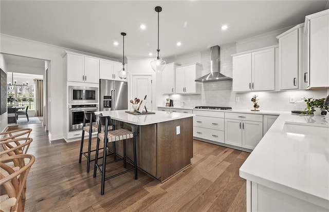 kitchen with stainless steel appliances, wall chimney range hood, white cabinets, and a center island