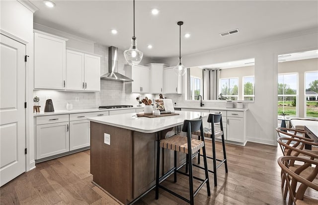 kitchen with white cabinets, pendant lighting, wall chimney range hood, and a kitchen island