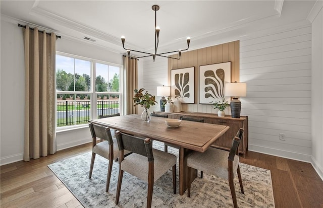 dining space featuring ornamental molding, a raised ceiling, light hardwood / wood-style floors, and a chandelier