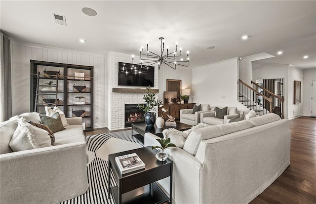 living room featuring a brick fireplace, dark wood-type flooring, a notable chandelier, and crown molding