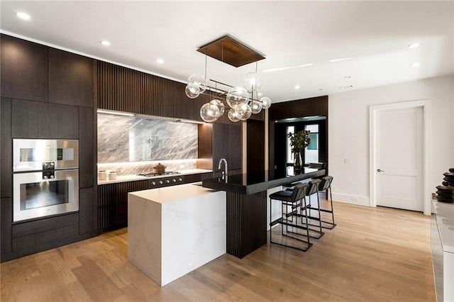 kitchen featuring sink, stainless steel appliances, light hardwood / wood-style flooring, an island with sink, and pendant lighting