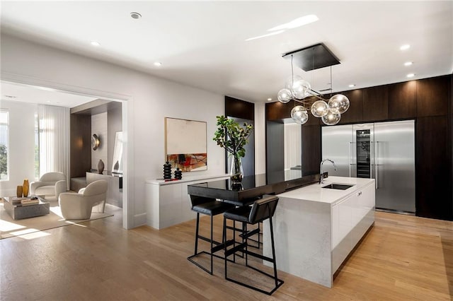 kitchen featuring white cabinetry, pendant lighting, a center island with sink, dark brown cabinets, and light wood-type flooring