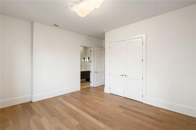 unfurnished bedroom with ensuite bath, a closet, and light wood-type flooring