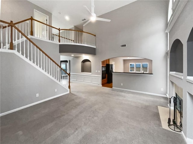 unfurnished living room featuring a fireplace with flush hearth, carpet, a towering ceiling, and stairs