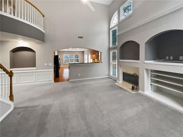 unfurnished living room with built in shelves, a fireplace with flush hearth, visible vents, stairs, and carpet