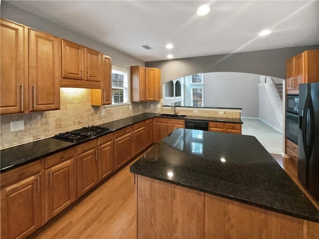 kitchen with arched walkways, a kitchen island, a sink, visible vents, and black appliances