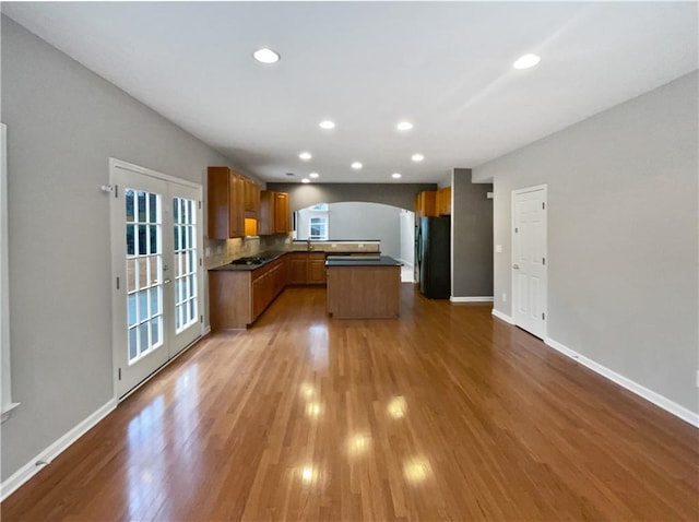 kitchen with arched walkways, wood finished floors, freestanding refrigerator, brown cabinets, and dark countertops