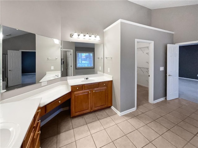 bathroom with a walk in closet, two vanities, vaulted ceiling, a sink, and tile patterned floors