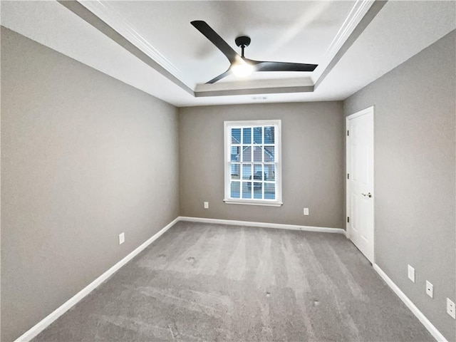 carpeted empty room featuring ceiling fan, baseboards, and a raised ceiling