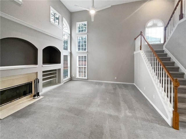 unfurnished living room featuring stairs, a wealth of natural light, carpet flooring, and a high end fireplace