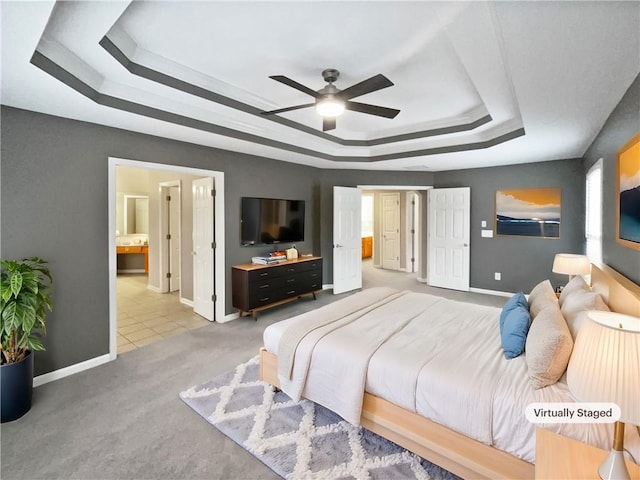 carpeted bedroom with ceiling fan, ensuite bath, a raised ceiling, and baseboards