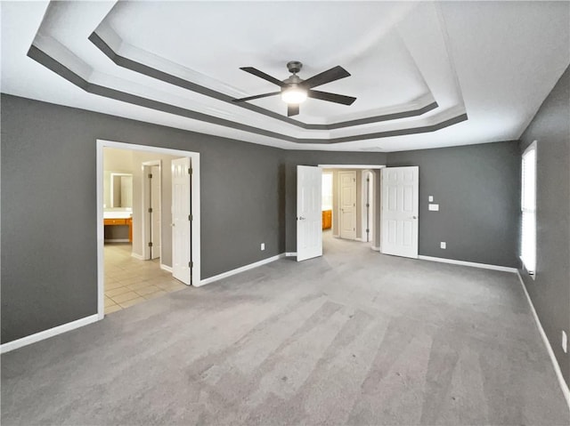 unfurnished bedroom with ensuite bathroom, carpet floors, a tray ceiling, and baseboards