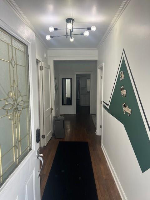 corridor with a notable chandelier, baseboards, wood finished floors, and crown molding