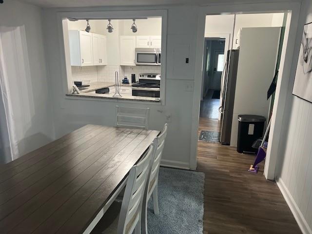 kitchen with dark wood finished floors, stainless steel appliances, backsplash, white cabinets, and baseboards