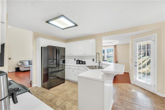 kitchen featuring a sink, white cabinetry, freestanding refrigerator, a peninsula, and light countertops