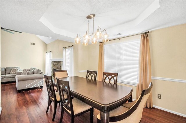 dining room with visible vents, a stone fireplace, an inviting chandelier, a textured ceiling, and dark wood-style flooring