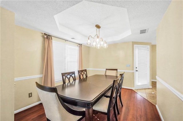 dining space featuring visible vents, a textured ceiling, wood finished floors, baseboards, and a raised ceiling