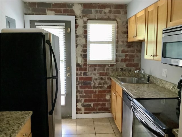 kitchen with appliances with stainless steel finishes, light stone counters, brick wall, light tile patterned floors, and sink