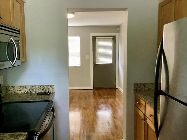 kitchen with appliances with stainless steel finishes, light hardwood / wood-style floors, and dark stone countertops