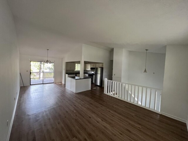 unfurnished living room featuring dark hardwood / wood-style flooring, vaulted ceiling, and a notable chandelier