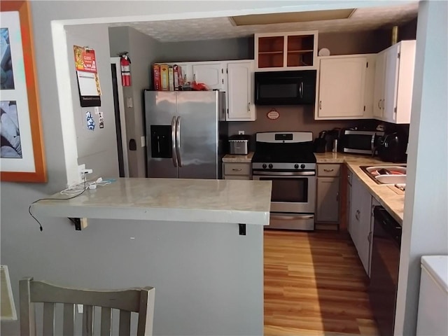 kitchen with light wood-type flooring, black appliances, kitchen peninsula, sink, and white cabinets