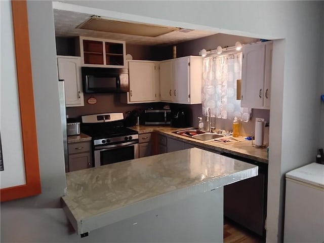 kitchen with appliances with stainless steel finishes, kitchen peninsula, white cabinetry, and sink