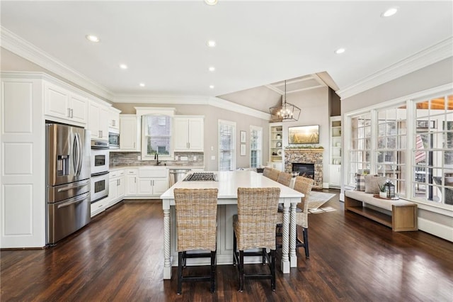 kitchen featuring stainless steel appliances, a fireplace, crown molding, a chandelier, and light countertops